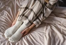 „ძილის ტაბუები“, რომელიც იღბლის მოზიდვაში დაგეხმარებათ – სპეციალისტის რჩევები Person sitting on a bed with white fluffy socks and plaid pajama pants, conveying coziness and relaxation.