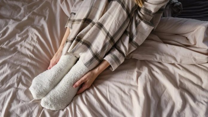 Person sitting on a bed with white fluffy socks and plaid pajama pants, conveying coziness and relaxation.